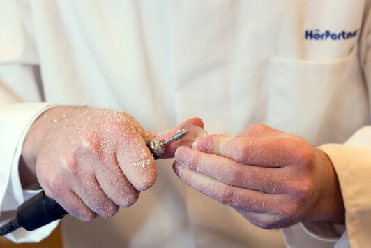 Ein Hörakustiker schleift ein individuelles Hörgerät in einer Fachwerkstatt.